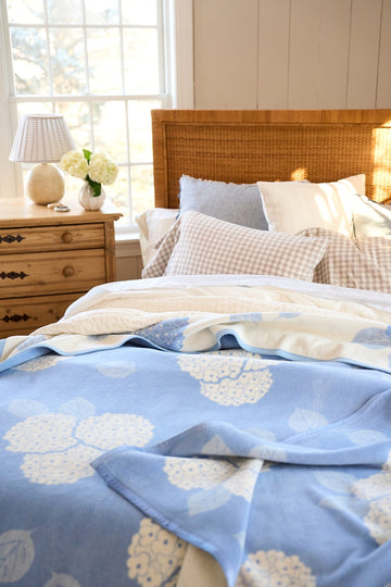 Blue and cream blanket with hydrangea flower pattern draped over a bed with pillows.5