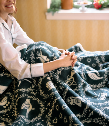 Dark blue blanket with white holiday motifs including partridges, pear trees, and numbered designs draped over a person's lap5