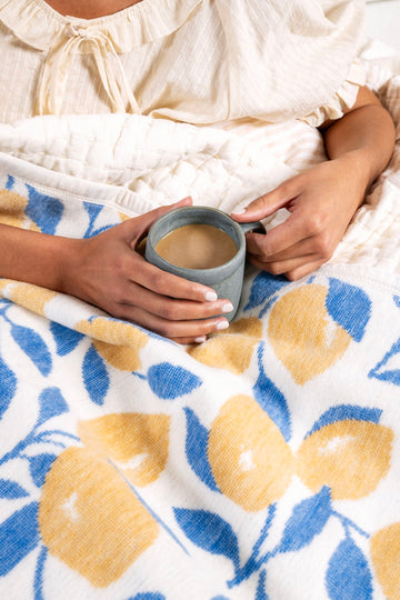 White blanket with blue and yellow lemon print held by person with gray mug.2
