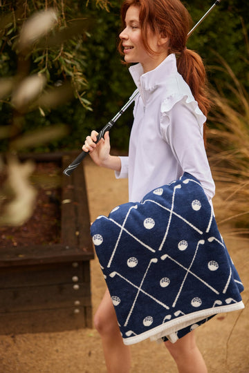 Navy blue blanket with golf club and ball pattern, cream trim, worn by person holding golf club outdoors.7