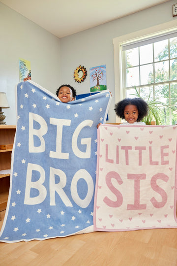 Blue blanket with "BIG BRO" text and white stars, displayed with child; pink "LITTLE SIS" blanket with hearts visible.5