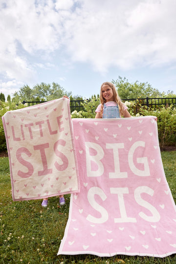 Pink blanket with "Big Sis" and "Little Sis" text and white heart pattern held by a young girl outdoors.6