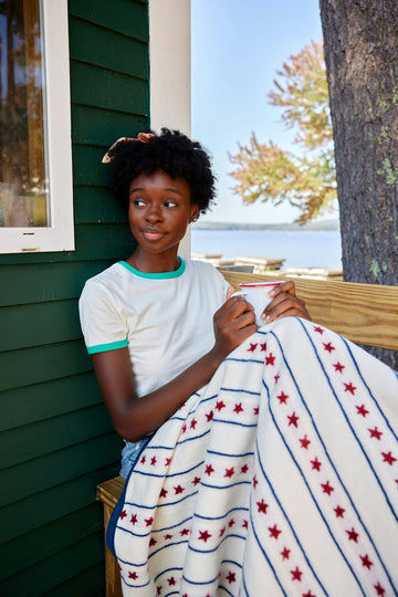 Cream-colored blanket with red stars and blue horizontal stripes draped over a person's lap outdoors.7