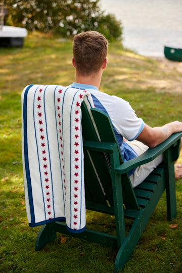 White blanket with red stars and blue stripes draped over a green Adirondack chair outdoors.6