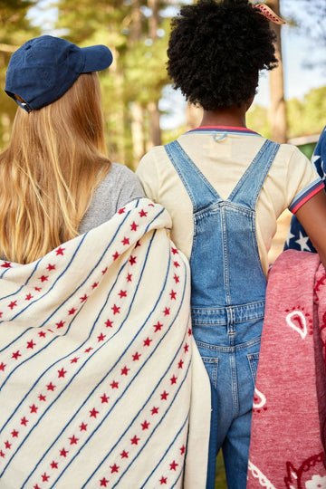Cream blanket with red stars and blue stripes draped over a child's shoulders outdoors.8