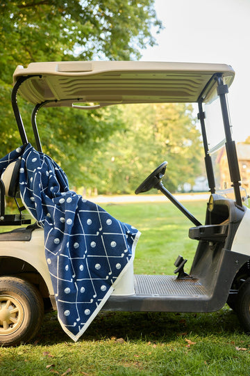 Navy blanket with white golf ball and line pattern draped over golf cart seat outdoors.4