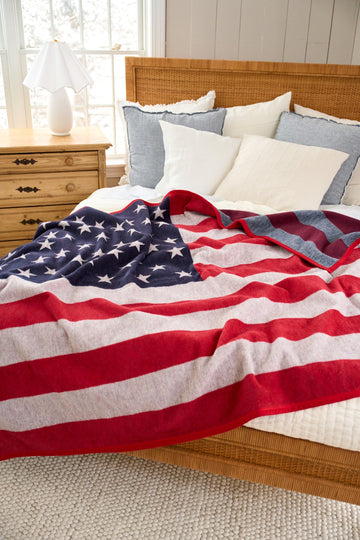 Red, white, and blue blanket with American flag design draped across a bed with pillows.8
