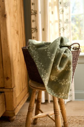 Sage green lightweight blanket with climbing ivy leaf pattern draped over wooden chair.3