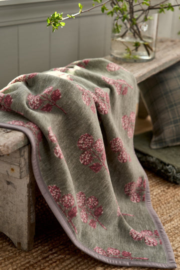 Cream blanket with pink hydrangea blockprint pattern draped over an upholstered chair.2
