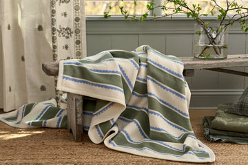 Striped blanket in cream, sage green, and blue draped over a wooden bench.7