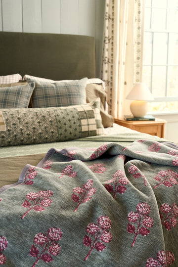 Gray blanket with pink and burgundy block-printed hydrangea flowers draped over a bed.3