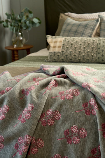 Beige linen blanket with red block-printed hydrangea flowers draped over a bed with matching pillows.6