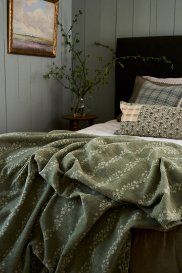 Sage green lightweight blanket with white leaf pattern draped over a bed in a bedroom setting.6