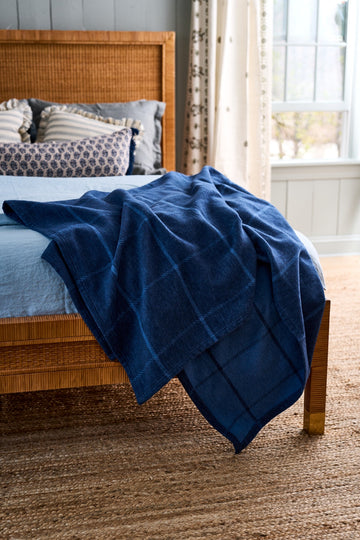 Navy blue windowpane quilted blanket draped over a wooden bed frame.4