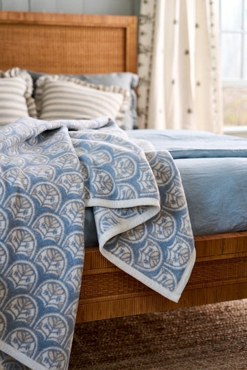 Blue and cream scallop-patterned blanket draped over a wooden bed with striped pillows.2