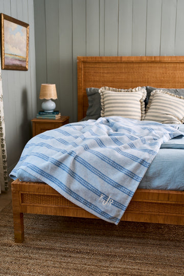 White and blue striped lightweight blanket draped across a wooden bed frame.3