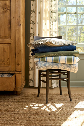 Stack of folded blankets in cream, tan, navy, and green tones with stripe and geometric patterns on wooden chair.5
