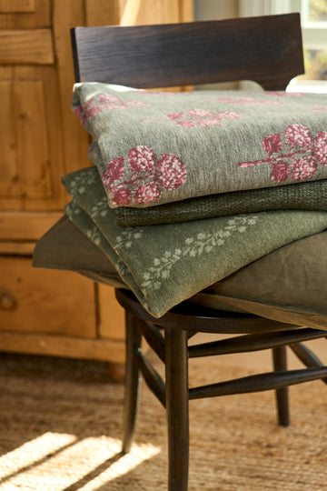 Folded blankets stacked on a wooden chair, with pink floral blockprint pattern on cream and solid sage green fabrics.8