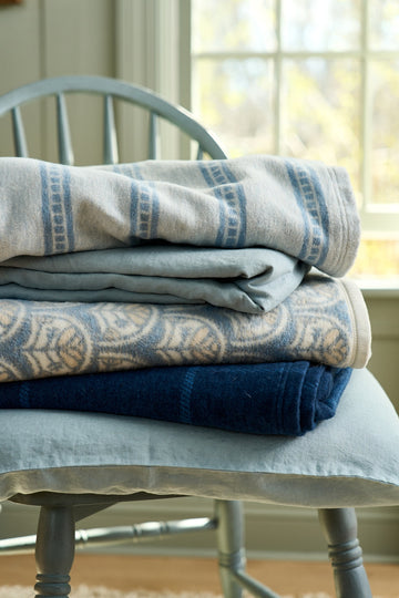 Stack of folded blankets featuring navy windowpane pattern and solid navy design on a light blue chair.5