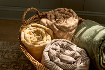 Rolled blankets in sepia and neutral tones displayed in a woven basket with herringbone weave pattern visible.4