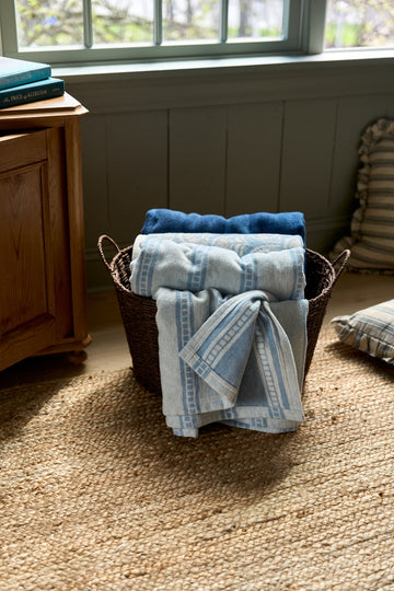 Lightweight blankets with blue and gray tile stripe pattern folded in woven basket.7
