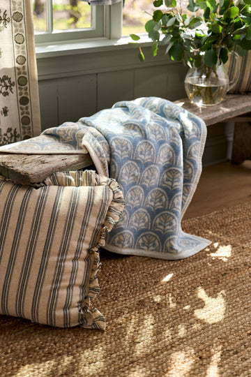 Blue and white scallop patterned blanket draped over a wooden log with striped pillows on a windowsill.7