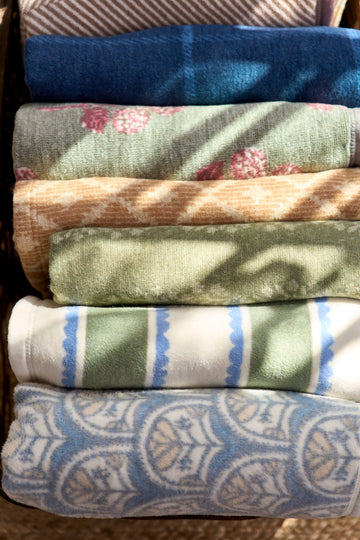 Stack of six folded blankets in blue, green, cream, and tan with various stripe and floral patterns.6