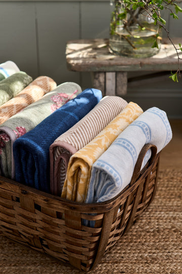 Rolled lightweight blankets in various colors and patterns displayed in a woven wooden basket.4