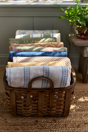Folded lightweight blankets in various stripe patterns and colors stacked in a woven wooden basket.8