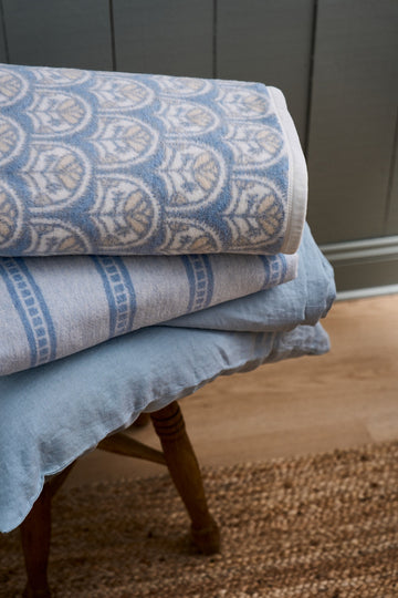 Stacked blue and cream blankets with scallop and striped patterns draped over a wooden chair.6