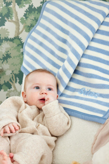 Blue and white striped mini blanket with bound edge displayed above infant in cream knit clothing.4