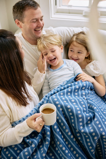 Blue and white patterned blanket with geometric design draped over a family sitting together on a bed.5