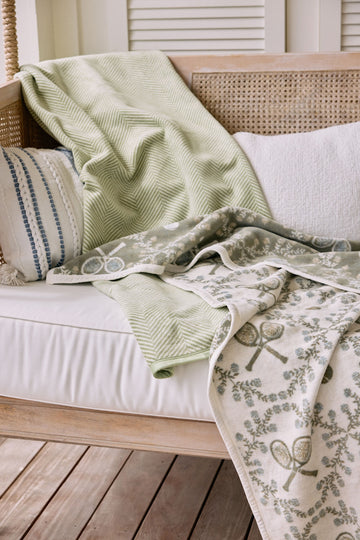 Light green herringbone blanket draped over cream sofa with matching botanical patterned throw.7
