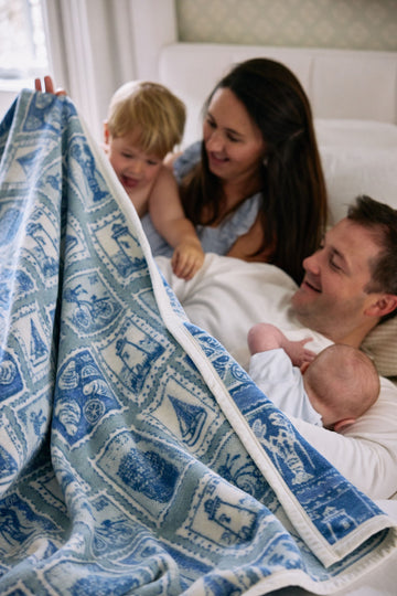 Blue and cream blanket with stamp-inspired patterns, held by adults and children on a couch.5
