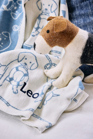 Cream and blue blanket with dog outlines and "Leo" text, displayed with brown and white plush dog toy.2