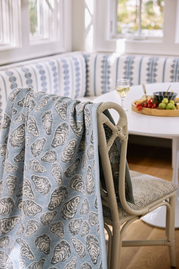 Blue and gray shell-patterned blanket draped over a chair with beige handles in a bright room.3