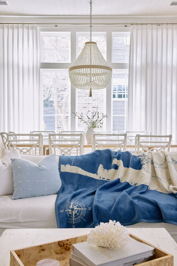Blue and cream blanket with map design and compass rose motif draped over white upholstered sofa.4