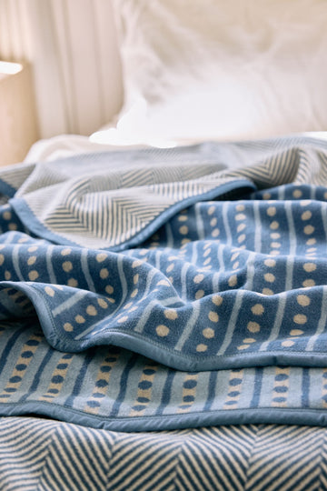 Blue and cream patterned blanket with geometric dot and stripe design draped on a bed.2
