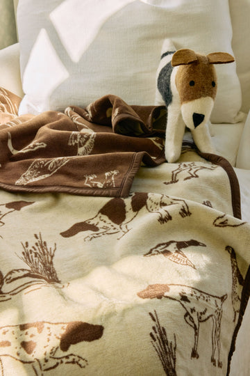 Cream and brown blanket with bird dog embroidered pattern, displayed with matching plush dog toy on white furniture.6