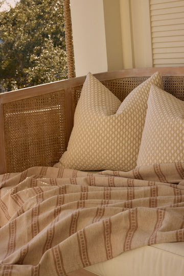 Tan lightweight blanket with vertical stripe pattern draped on bed with matching pillows.5