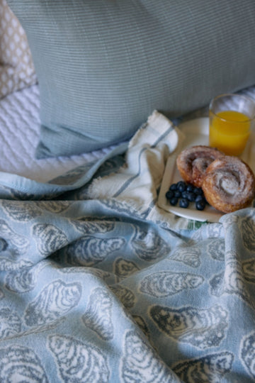 Blue and cream blanket with shell pattern displayed on bed with striped pillow and breakfast items.5
