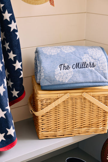 Light blue blanket with white floral pattern and "The Millers" embroidered text, folded in wicker basket.6