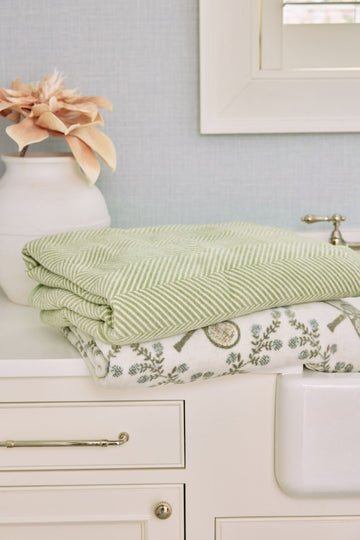 Folded green and white herringbone blanket displayed on bathroom vanity next to floral patterned fabric.2