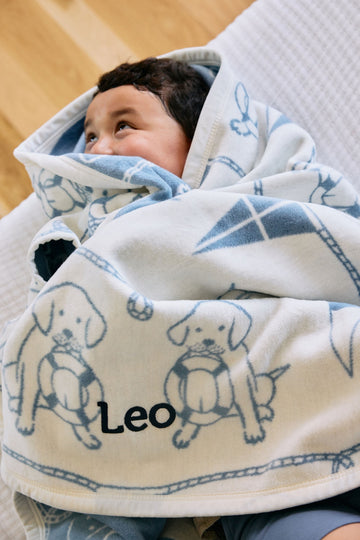 Cream and blue blanket with sailor dog print and personalization, wrapped around a child.5