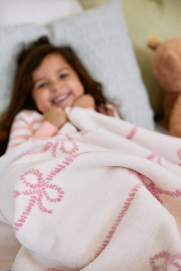 White and pink midi blanket with embroidered bow pattern, held by child and adult.5