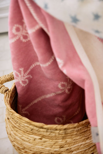 Pink midi blanket with buoy bow pattern draped in woven basket.6