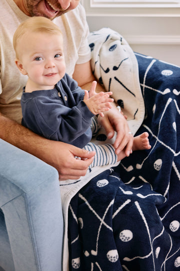 Man holding toddler with navy and cream golf-patterned blanket featuring clubs, balls, and flag designs.2