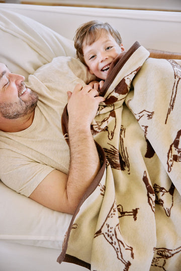 Cream and brown blanket with bird dog pattern, held by adult and child on bed.4