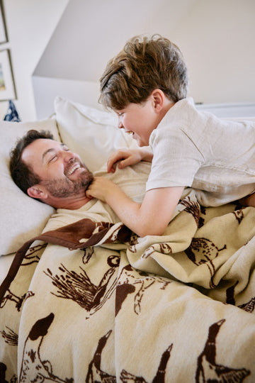 Cream-colored blanket with brown bird and wildlife print, draped over an adult and child on a bed.2
