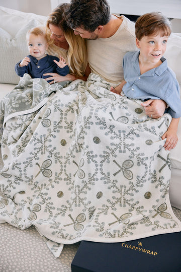 Cream blanket with sage green tennis racket and floral pattern, displayed on bed with family.4